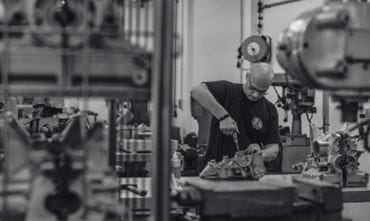 Photo noir et blanc d'un homme en train de réparer un moteur à la main dans un atelier