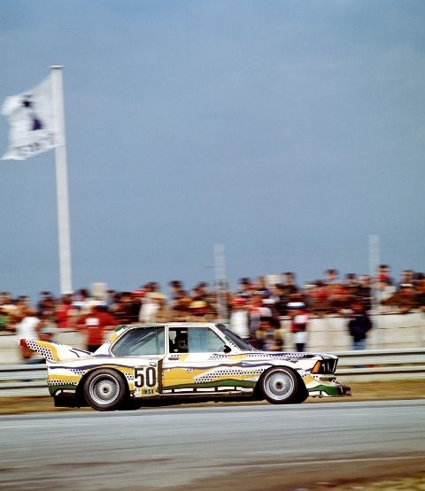 BMW de course aux couleurs vives, en action sur une piste avec des spectateurs en arrière-plan.