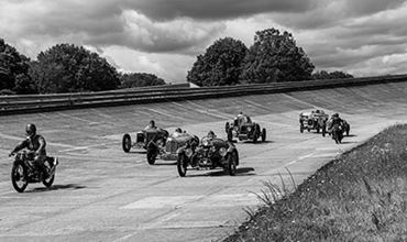 Photo noir et blanc de voitures et motos de collections roulant sur l'anneau de vitesse de l'autodrome UTAC Linas Montlhéry