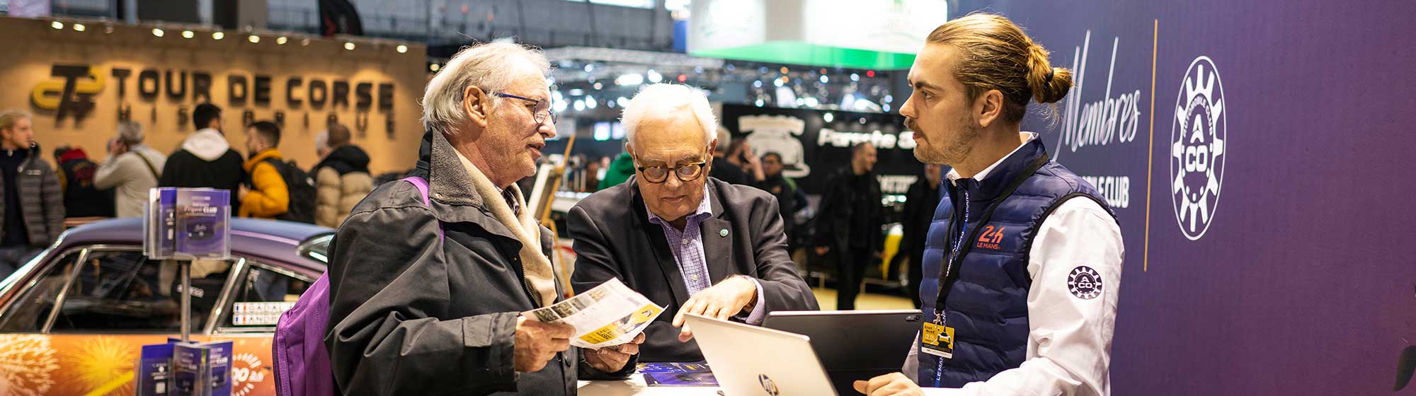 Photo d'un exposant à Rétromobile discutant avec deux visiteurs sur son stand