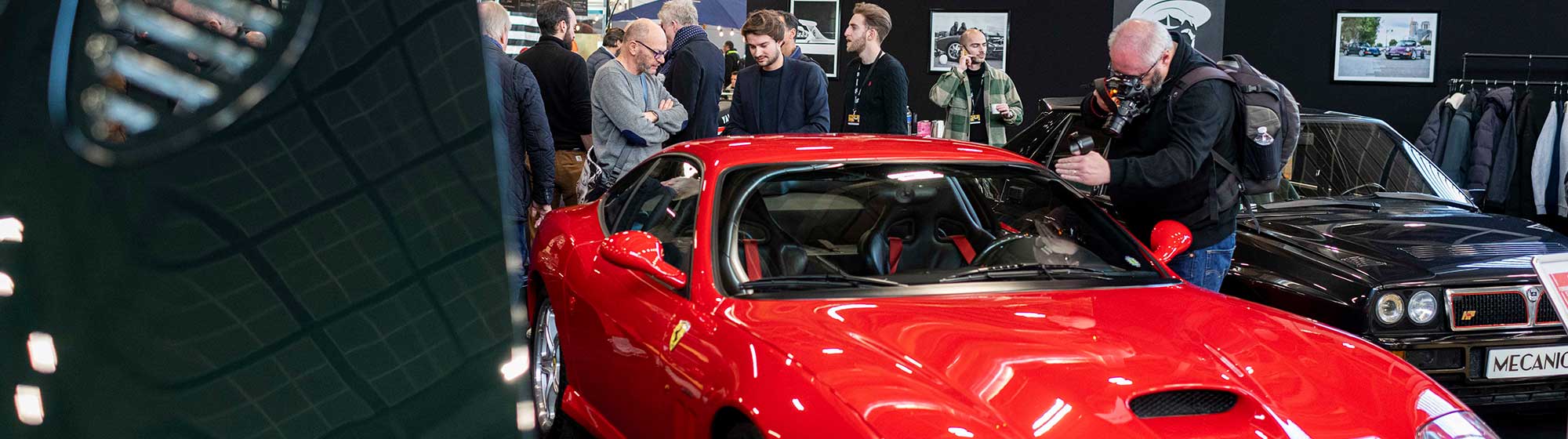 Group of men admiring a red car on a stand at Rétromobile