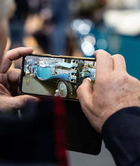 close-up of hand holding a phone, taking a picture of blue car